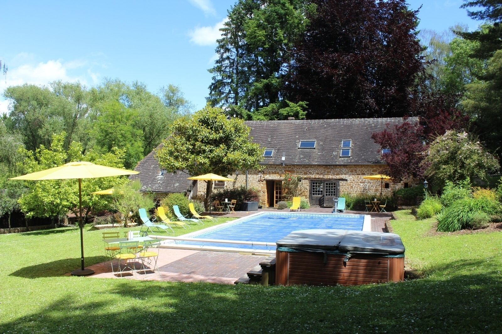 Un espace piscine avec des chaises longues et des parasols, un jacuzzi et un bâtiment en pierre doté d’un jardin.