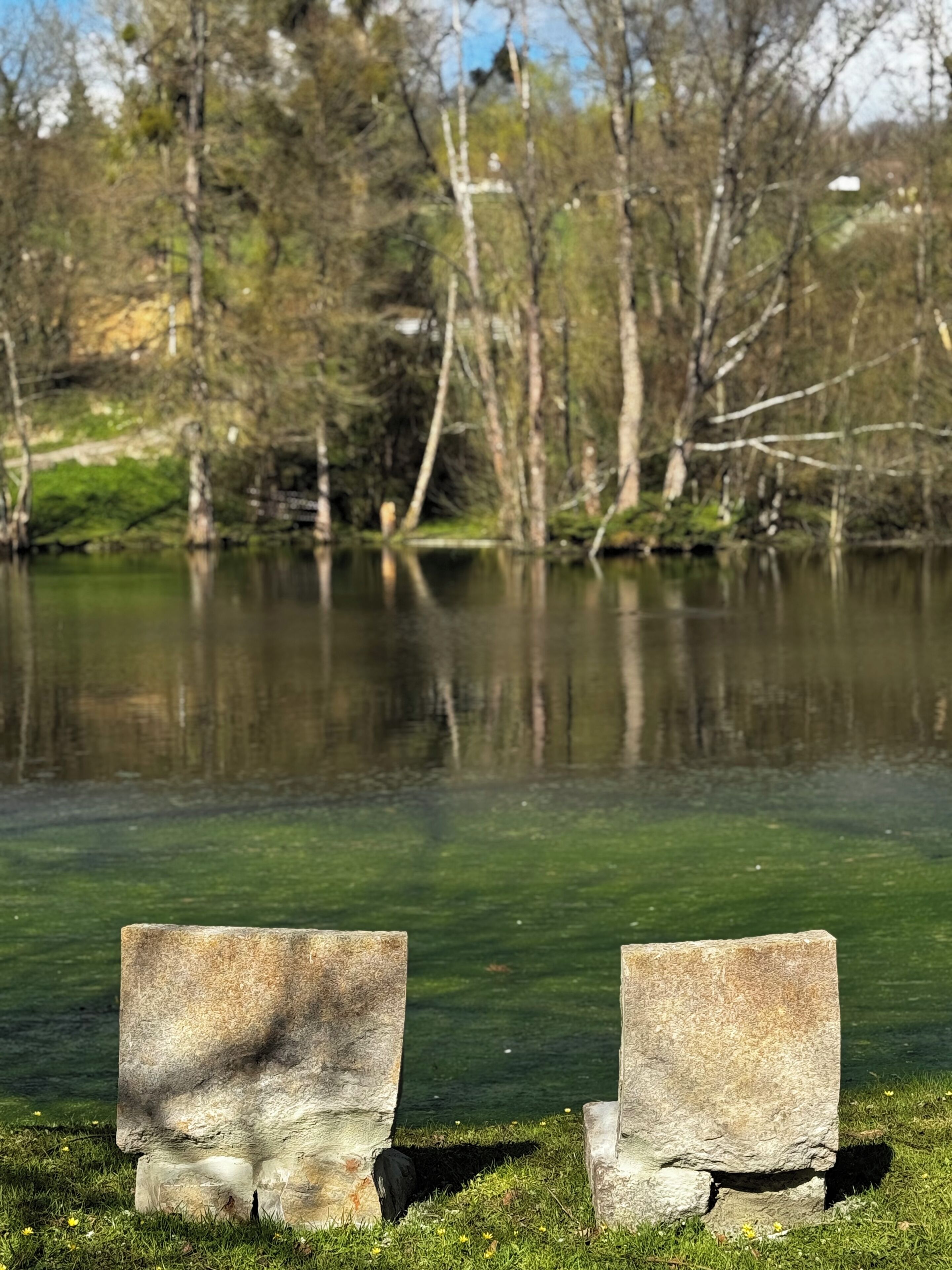A stone bench by a clear lake with trees in the background.