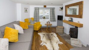 Una sala de estar con un sofá gris, cojines amarillos, un manto de piel, un sillón amarillo, una pequeña mesa de madera y una chimenea.
