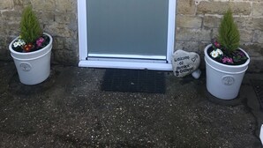 Una puerta gris con un llamador con forma de corazón, un buzón y un cartel de bienvenida a Marrock Cottage.