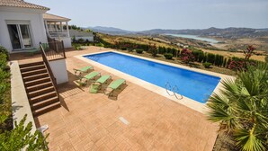 Ein Pool mit Blick auf Berge und einen See, umgeben von einer Terrasse mit Liegestühlen und einer Treppe zu einem überdachten Bereich.