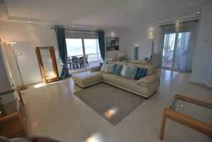 Ein geräumiges Wohnzimmer mit einer großen Eckcouch, einem Glastisch und einem Balkon mit Blick.