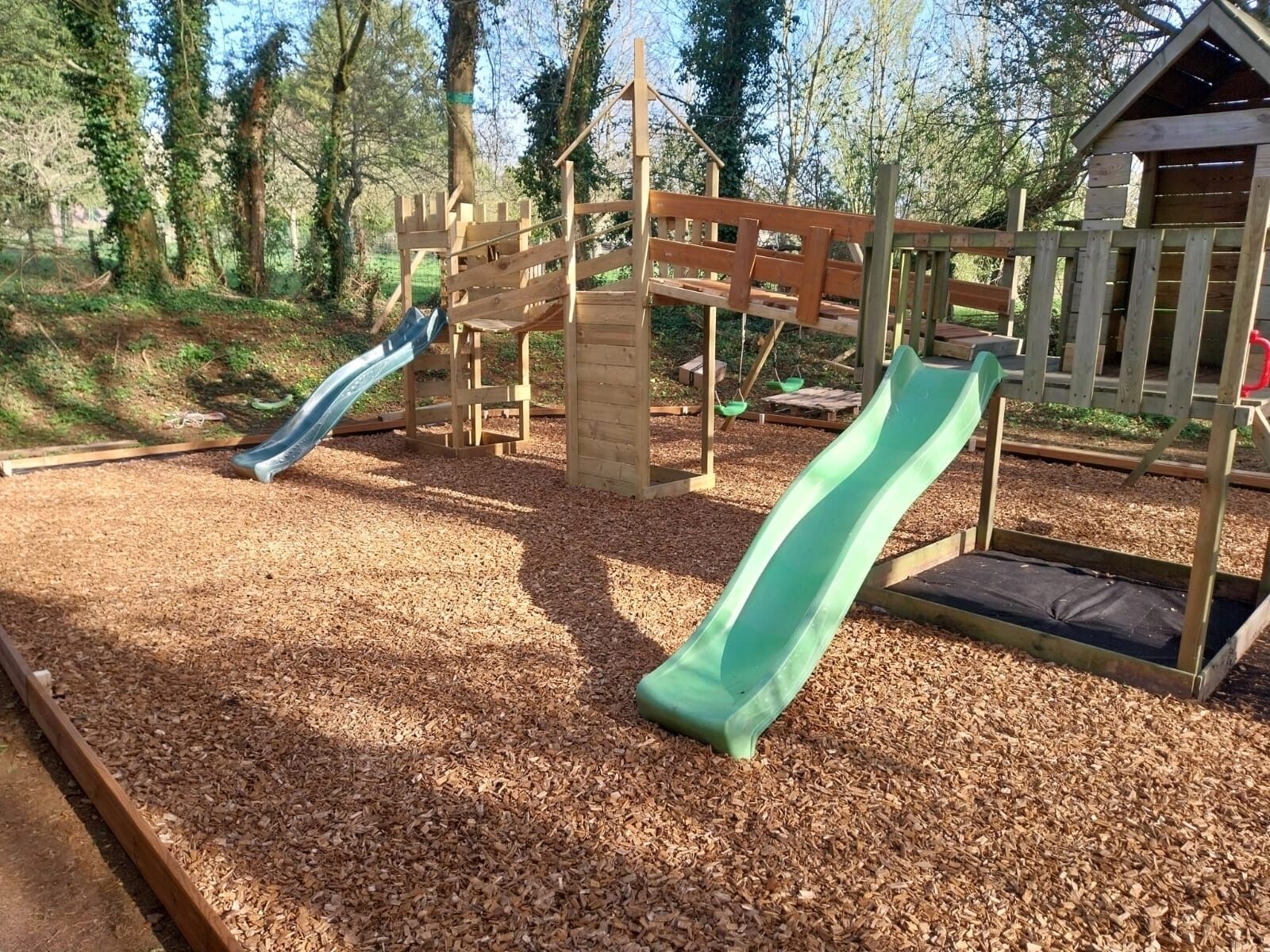 Une aire de jeux avec deux toboggans et une cabane en bois.