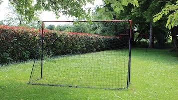 A soccer goal in a grassy area with a hedge and trees in the background.