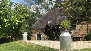 A stone house with a tiled roof, a gravel pathway, and two large metal vases. - Cottage with shared swimming pool, hot tub, fishing, tennis, UK TV and Wi-F (Guerquesalles)