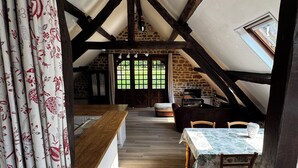 An attic room with a wooden staircase, a dining table with chairs, and a view of the garden through a window. - Cottage with shared swimming pool, hot tub, fishing, tennis, UK TV and Wi-F (Guerquesalles)
