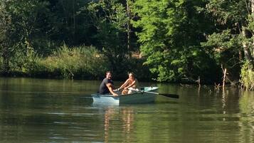 Two people rowing a small boat on a calm lake surrounded by dense trees.