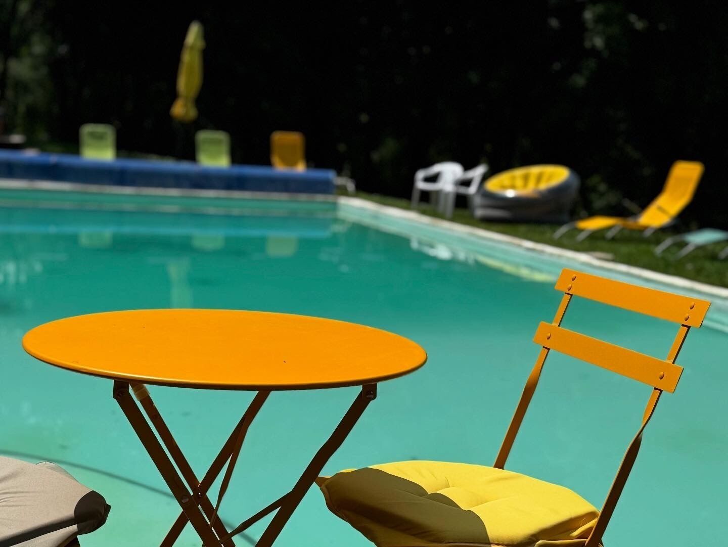 Een zwembadterras met een tafel en stoelen, een zwembad en een gazon met gele ligbedden.