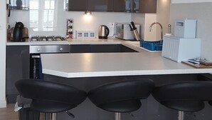 A modern kitchen with a central island, bar stools, stainless steel appliances, and a window overlooking a balcony. - Cultural Heart of Margate (Margate)