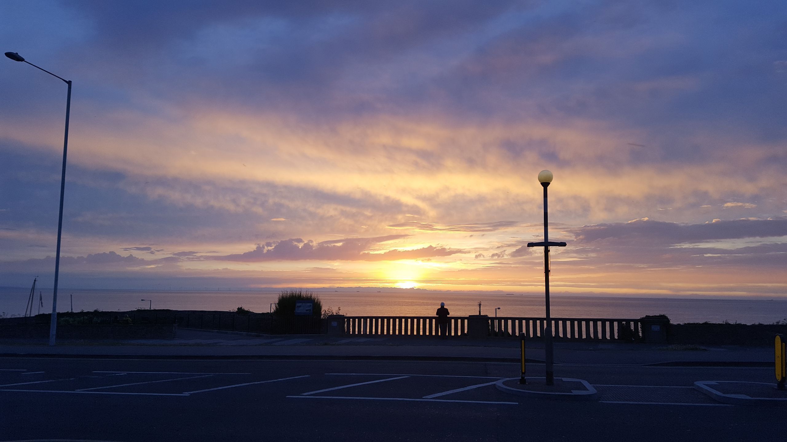 A sunset over a body of water with a bridge and street lamps.