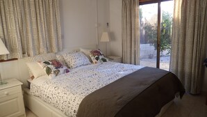 Een slaapkamer met een bed, nachtkastje, lamp en gordijnen.