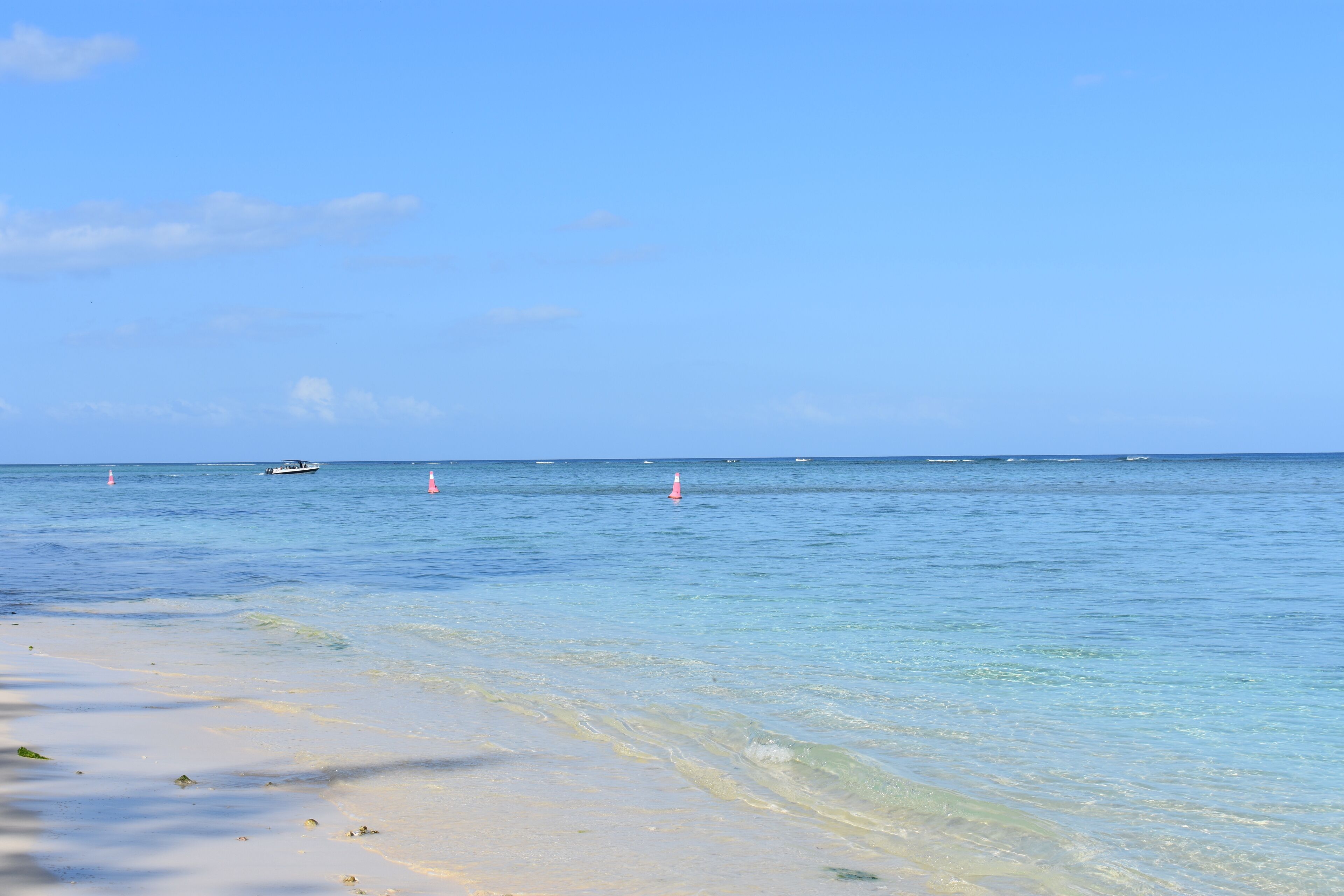 Ein Strand mit klarem Wasser, einem sandigen Ufer und ein paar Booten in der Ferne.