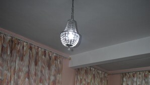 A dining room with a round table, six wooden chairs, a chandelier, and patterned curtains. - Bungalow - Feet in the water (Flic En Flac)