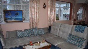 A living room with a grey sofa, patterned cushions, a coffee table with books and flowers, and a painting of a beach scene. - Bungalow - Feet in the water (Flic En Flac)