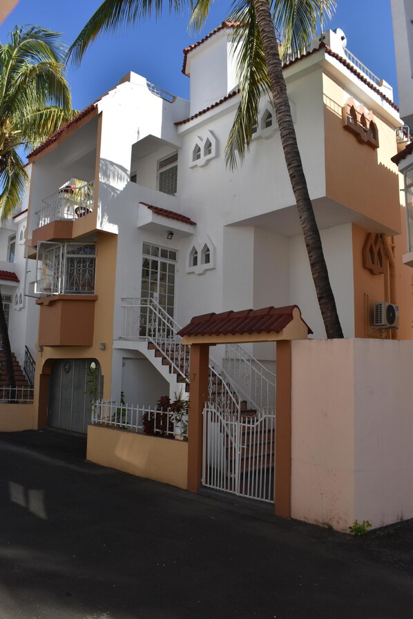 A multi-story residential building with balconies, a gated entrance, and a staircase leading to the upper floors.