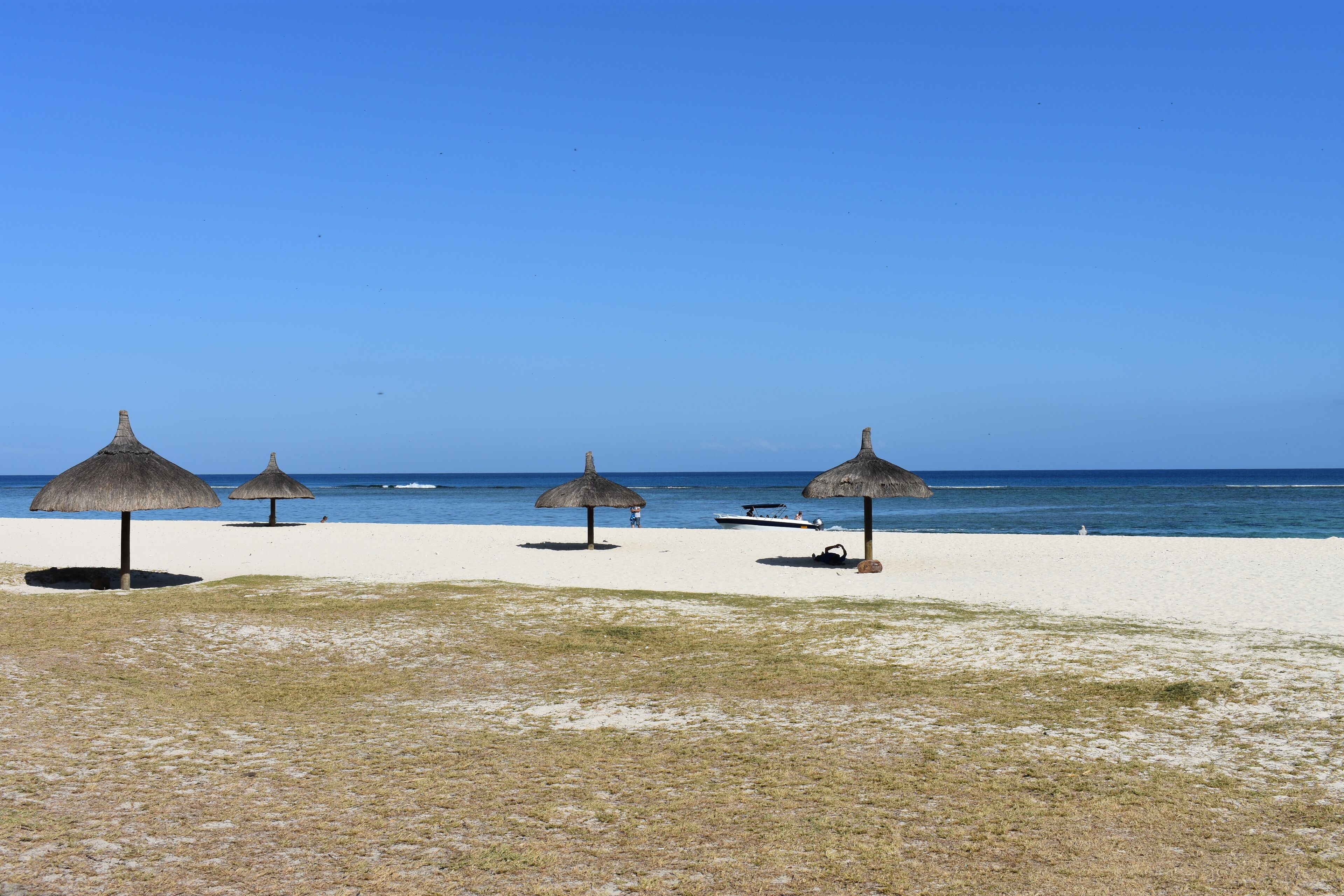 A beach with four thatched umbrellas and a boat on the sand.