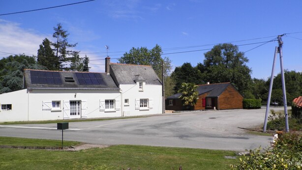 A two-story building with a solar panel on the roof, a small attached structure, and a clear sky. - Au Bas Chalonge l'Appart (Ligné)