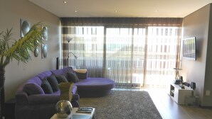 Een moderne woonkamer met een gebogen paarse bank, een klein wit tafeltje en een grote potplant.