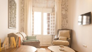 A cozy living room with a stone wall, a sofa, a chair, a coffee table, and a TV mounted on the wall.