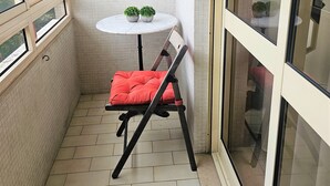 A small balcony with a tiled floor, a round table with two potted plants, a red cushioned chair, and a sliding glass door. - Lucinda's House. Welcome (BRAGA)