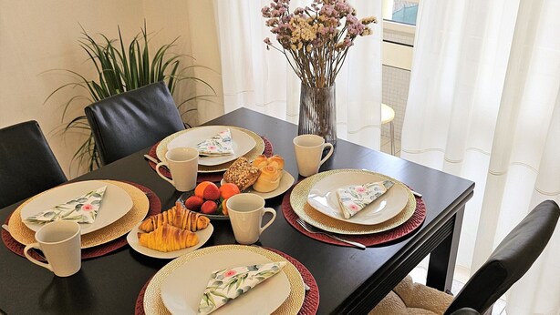 A dining table set with plates, cutlery, a vase with flowers, and a plant. - Lucinda's House. Welcome (BRAGA)