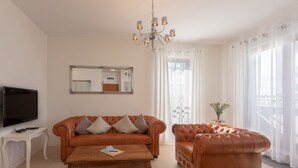 Un salon comprenant un canapé, un fauteuil, une table basse, un téléviseur et un lustre.