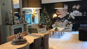 A modern living room with a dining area, featuring a Christmas tree, wicker furniture, and a large mirror.