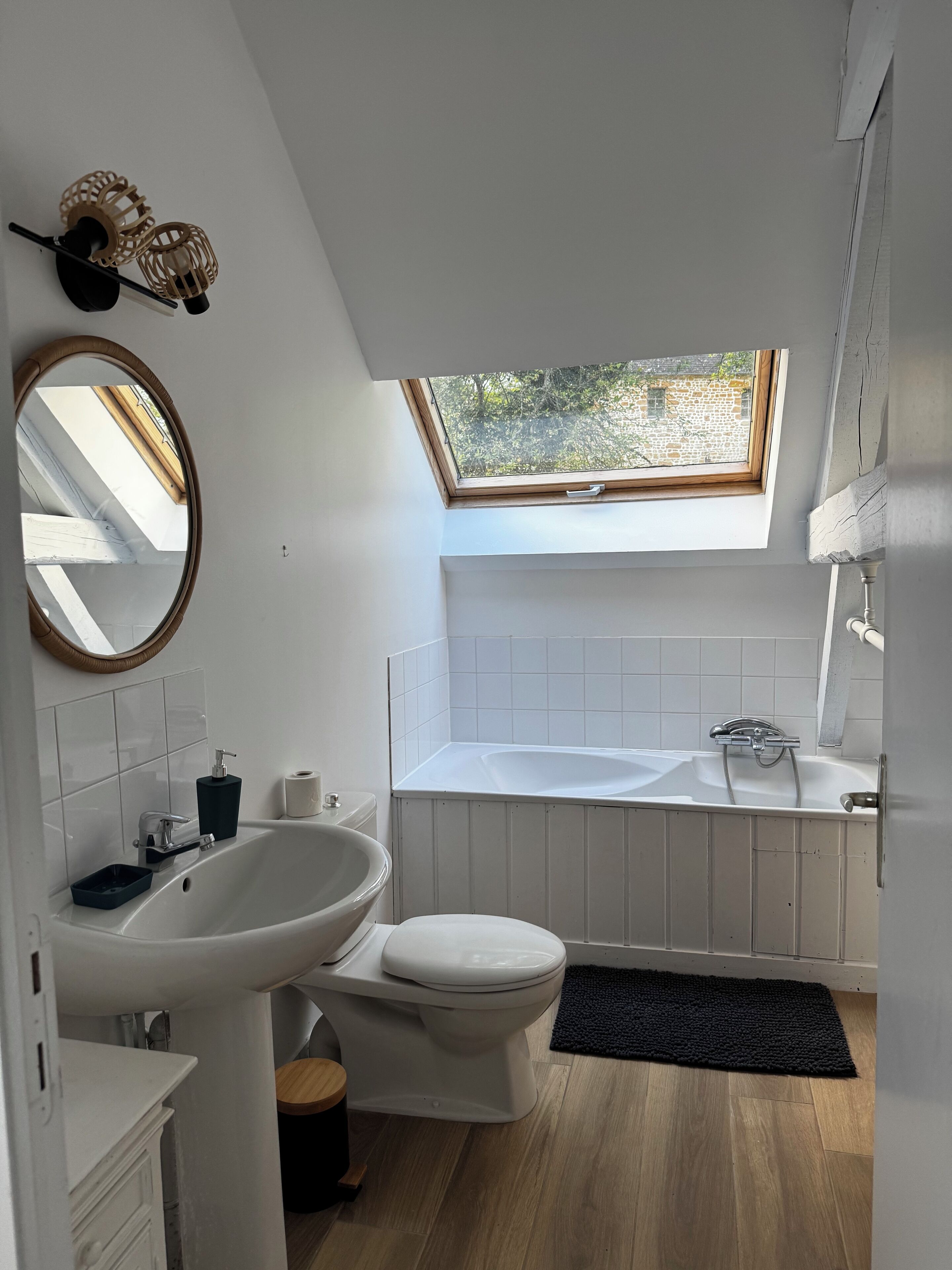 A modern bathroom with a skylight, white fixtures, and a wooden floor.