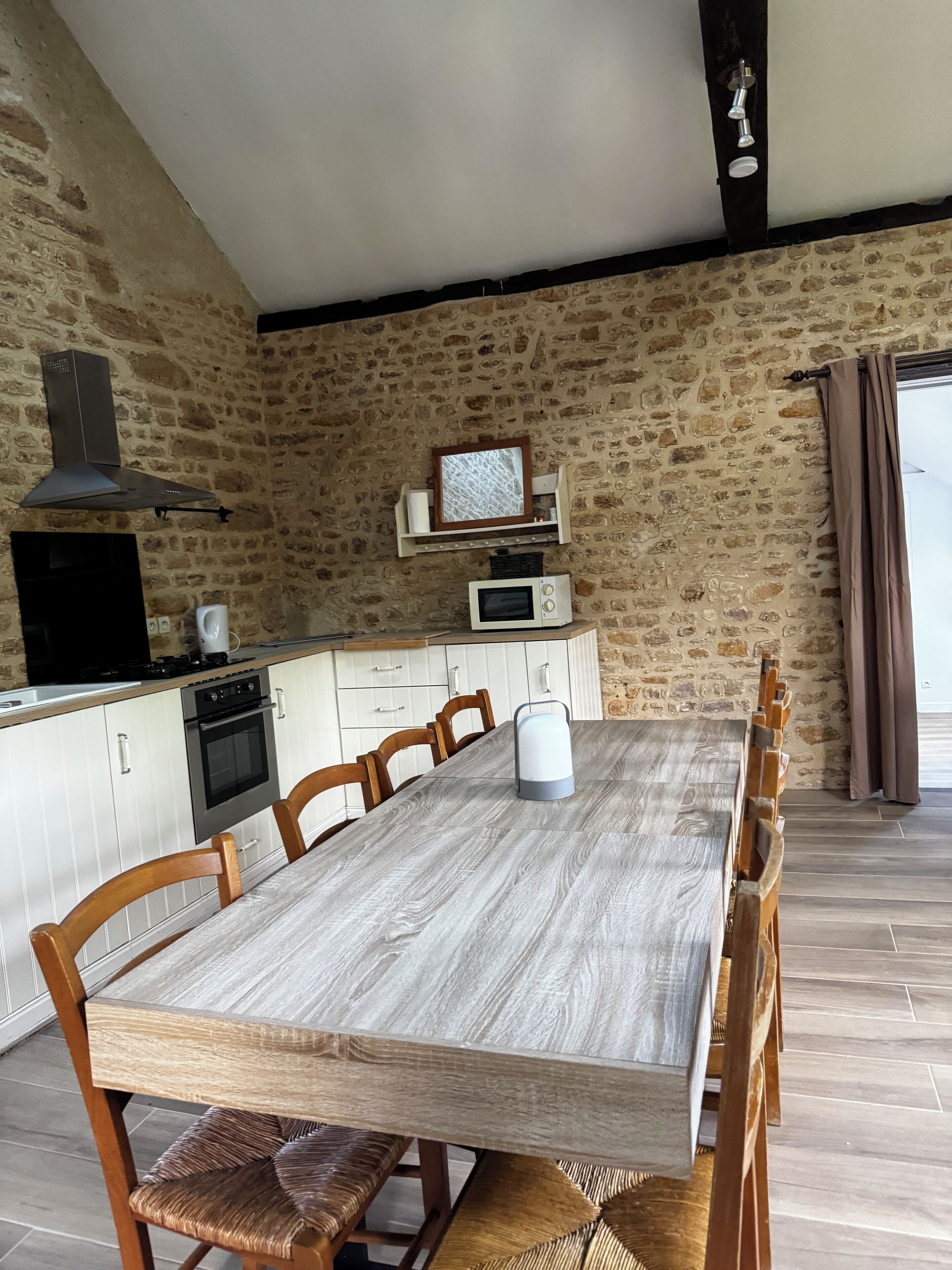 Une cuisine avec un mur en pierre, une table à manger en bois et un four à micro-ondes moderne.