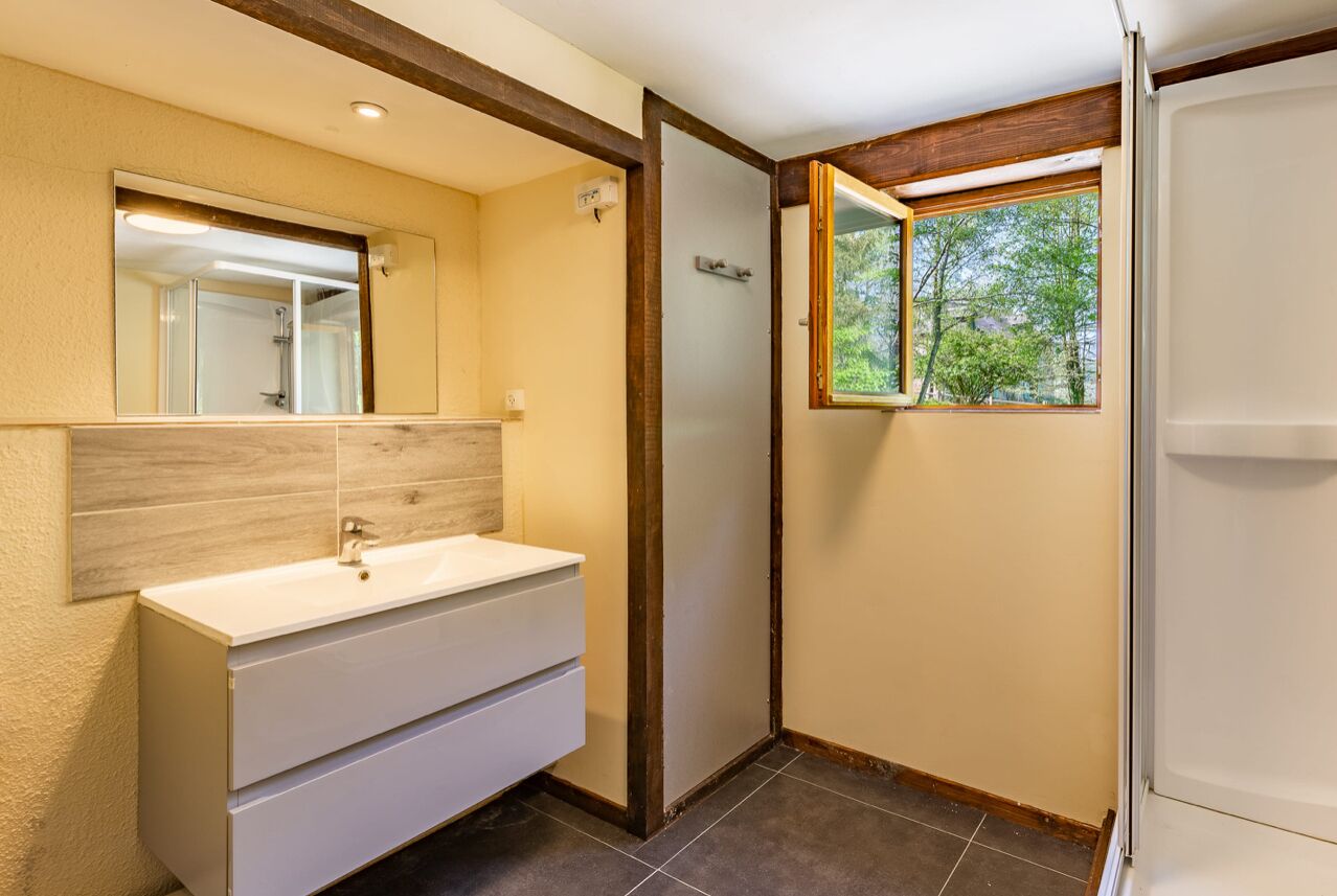 Une salle de bain avec un meuble-lavabo blanc, un miroir et une fenêtre donnant sur des arbres.