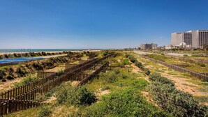 Una zona costera con playa de arena, cerca hay una valla de madera y una piscina.