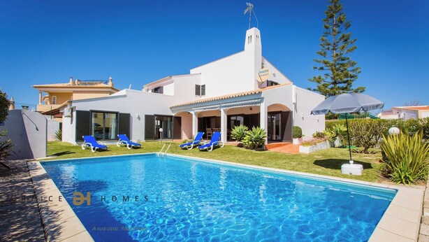 Una casa moderna con piscina, sillas de descanso azules y un jardín bien cuidado.