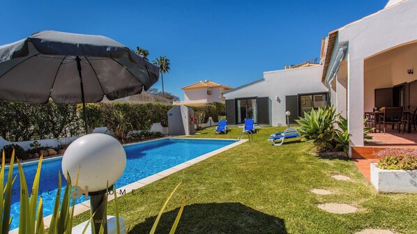 Ein modernes Haus mit Swimmingpool, einer Terrasse mit Stühlen und einem gepflegten Rasen.