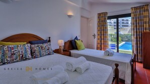 Habitación de hotel con dos camas, una mesita de noche con lámpara, vista a una piscina y un balcón con cortinas.