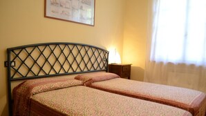 A room with two beds, a headboard, a nightstand, a lamp, and a window with curtains. - Detached villa 50 meters from the sea (Isola d'Elba)