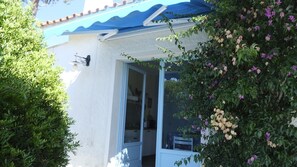 Uma casa com toldo azul, porta de vidro e um jardim com várias plantas e flores.