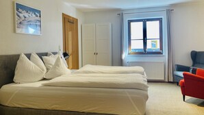 Ein Hotelzimmer mit Bett, Stuhl, Fenster, Tür und einem Bild an der Wand.