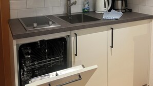 Eine kleine Küche mit weißen Schränken, einer Edelstahl-Spüle, einer Kaffeemaschine und einem Geschirrspüler.