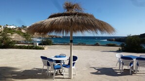 Un espace extérieur aménagé avec une table et des chaises, un parasol en chaume et une vue sur la mer.