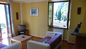 Un salon confortable avec un canapé, une petite table, un téléviseur et une fenêtre donnant sur des arbres et des immeubles.