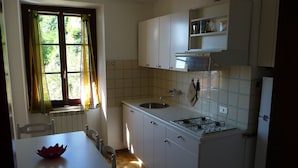 Une cuisine avec des meubles blancs, une cuisinière, un évier et une fenêtre avec des rideaux.