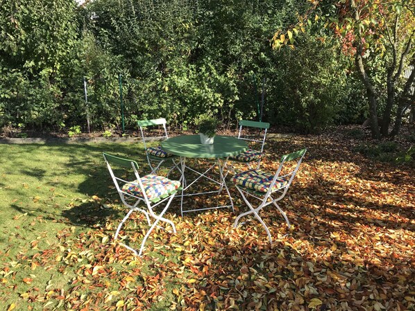 A round table with four chairs, surrounded by a grassy area with scattered fallen leaves. - Comfortably furnished apartment in Pastetten district Erding (Pastetten)