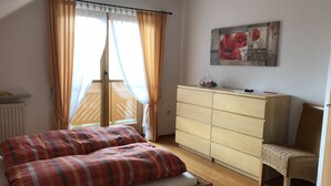 A bedroom with a bed, a dresser, a chair, and a window with curtains. - Comfortably furnished apartment in Pastetten district Erding (Pastetten)