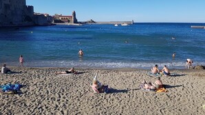 Ein sandiger Strand mit badenden und sonnenden Menschen.