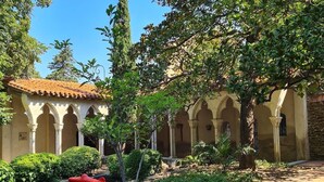 Ein Innenhof mit einem Gebäude mit Ziegeldach, Säulen und üppigem Grün.