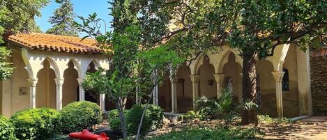 A courtyard with a tiled-roof building, columns, and lush greenery.