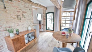 Una habitación acogedora con una mesa de comedor de madera, una silla azul, un aparador de madera con vajilla y una pared de ladrillo.
