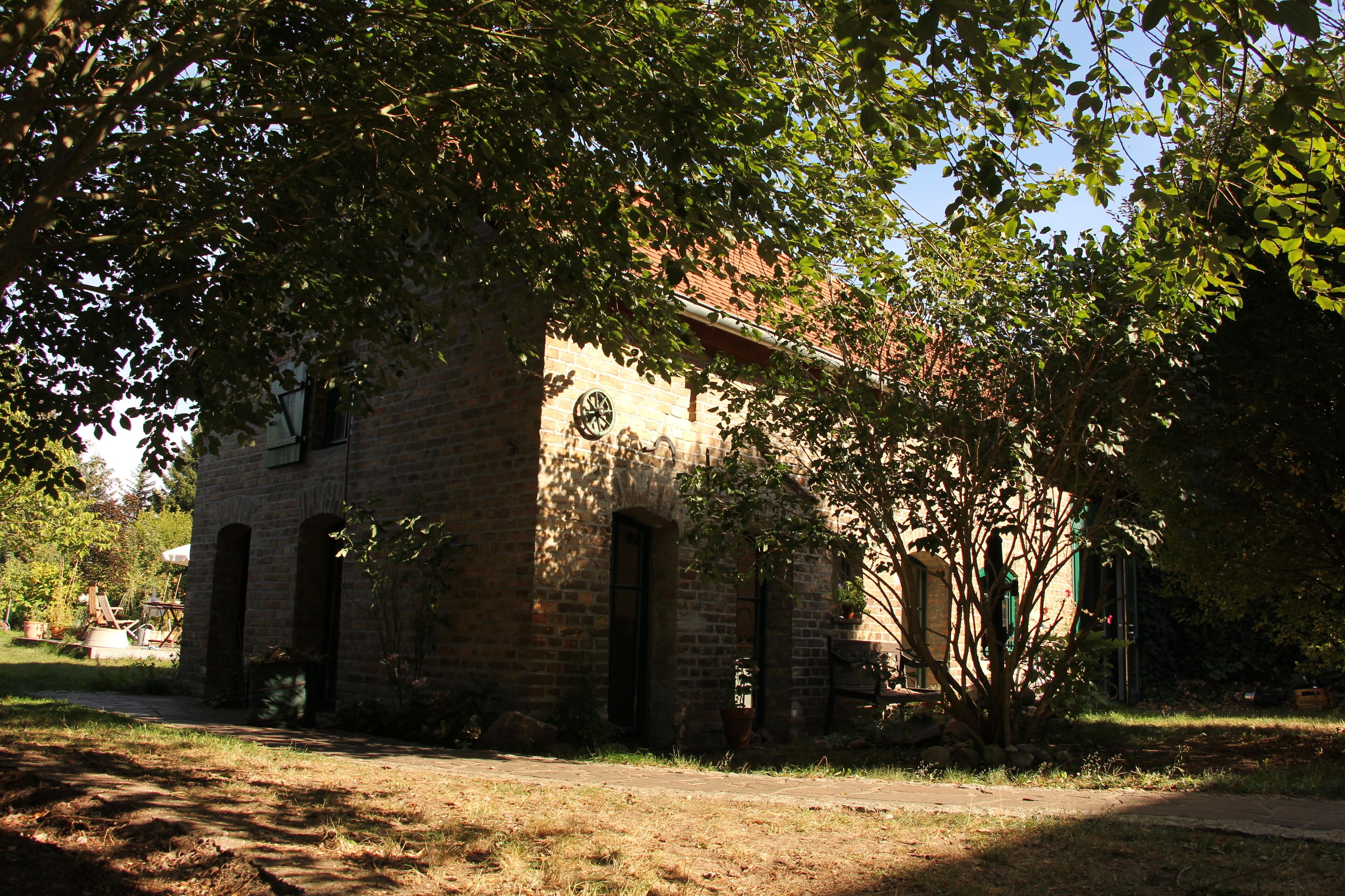 A brick building with arched doorways, surrounded by trees and a clear sky.