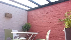 A patio area with a red brick wall, a white table, and two green chairs. - Apartment with patio, quiet, near the market and in the city center (Dinard)