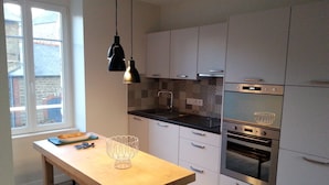 A modern kitchen with white cabinets, a wooden table, and two pendant lights. - Apartment with patio, quiet, near the market and in the city center (Dinard)